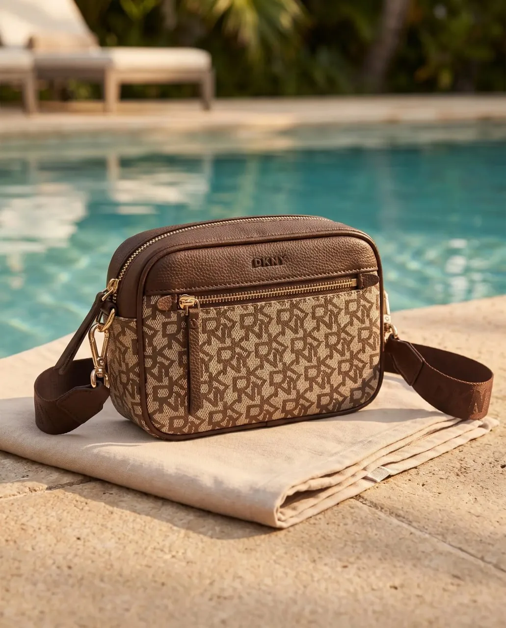 Sac DKNY chocolat monogramme posé au bord de la piscine